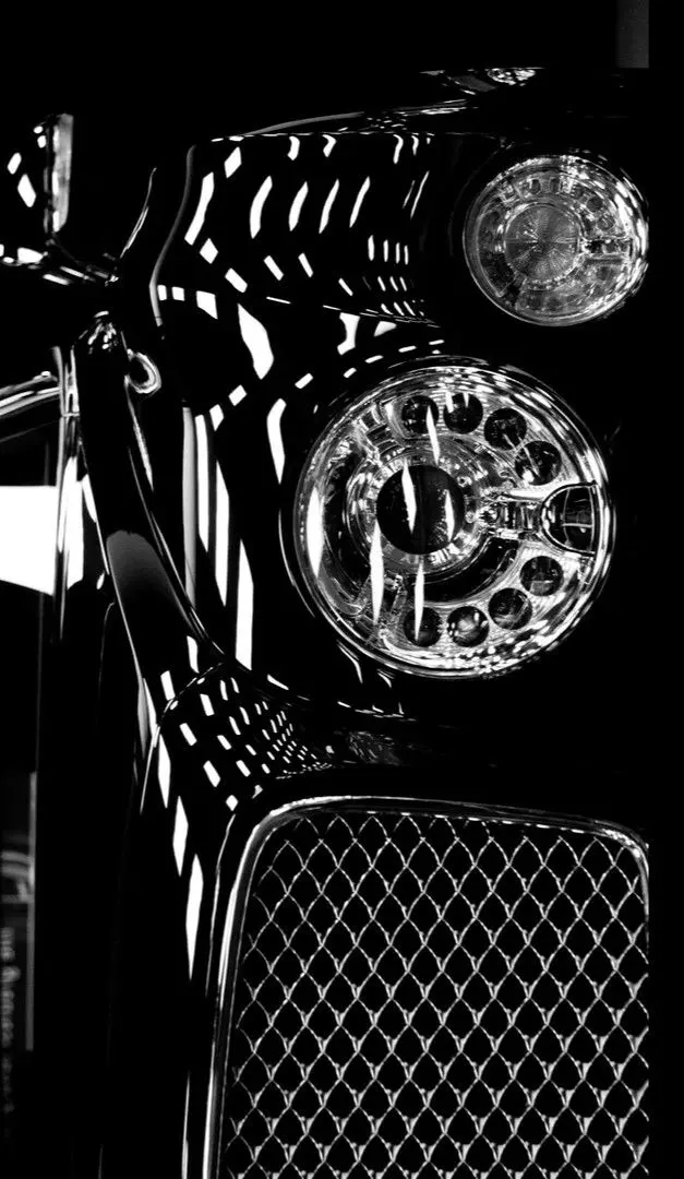 A black Bentley's twin circular headlights and mesh grille in reflected light