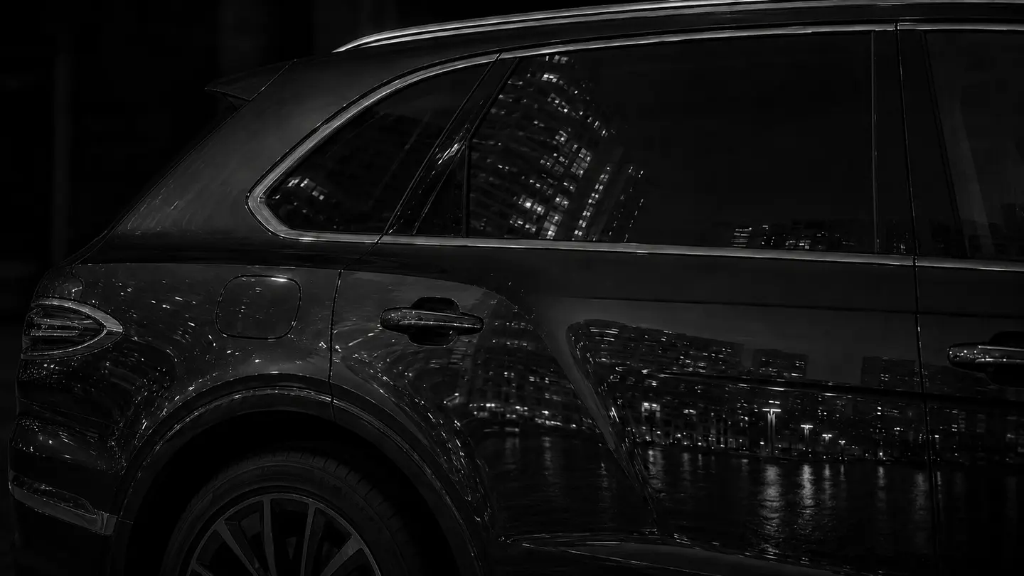 The outlined rear door of a Bentayga carrying city reflections across its black paint