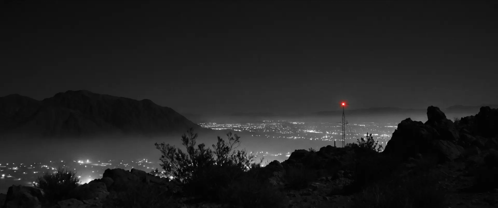 Las Vegas observed from the quiet desert threshold, with a single red tower beacon