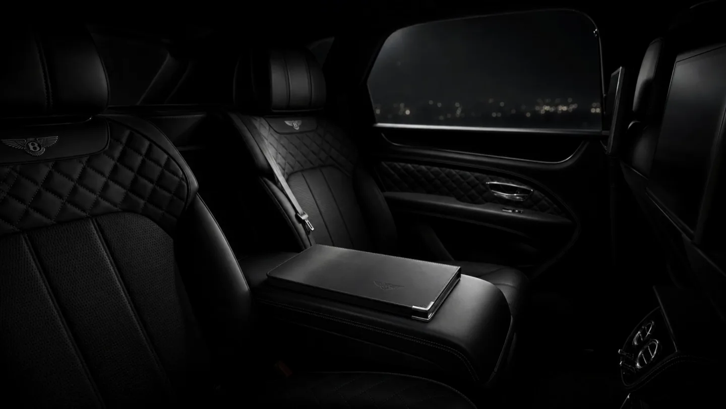 An empty private Bentayga rear cabin holding a closed folio while passing light moves across the leather
